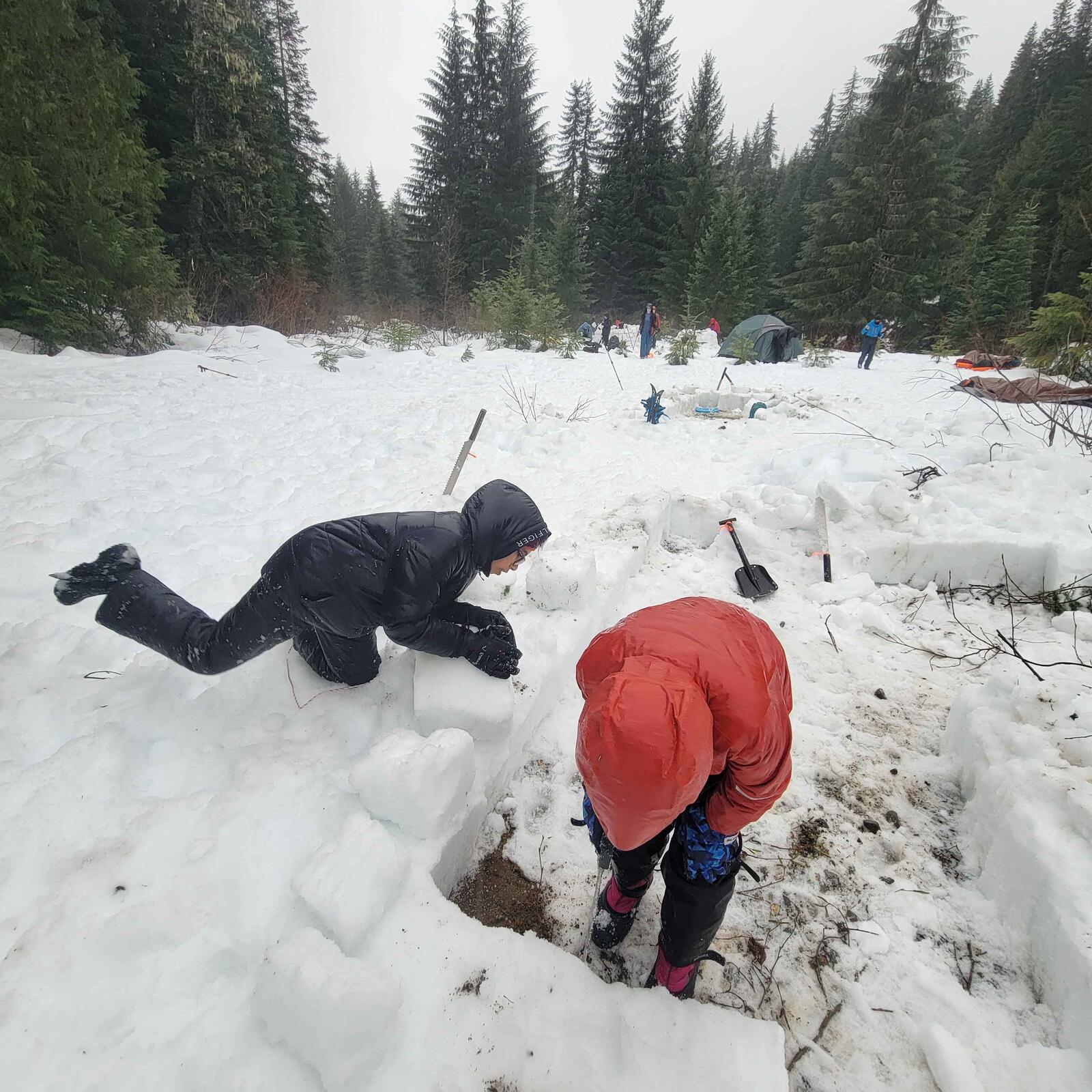 Two scouts digging out the entrance to a snow igloo